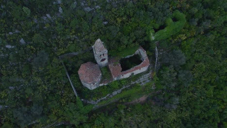 Top-down-of-ruined-church-on-lush-green-mountain-during-day-time-at-Kotor-bay,-aerial