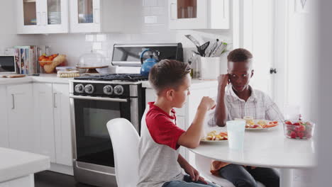 Two-pre-teen-male-friends-sit-talking-in-the-kitchen-during-a-playdate-at-one-boy’s-house