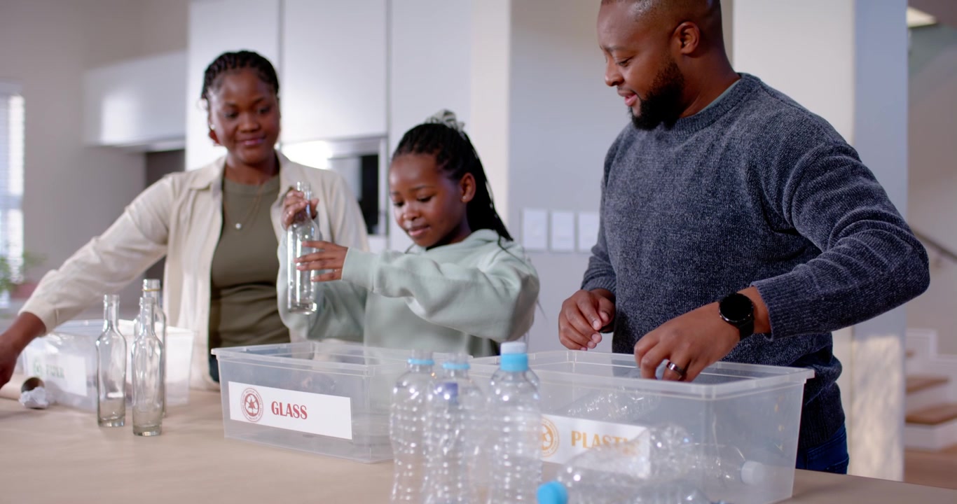 Family at kitchen table prompted by bottle pile, sorting into PLASTIC and GLASS bins, guiding child