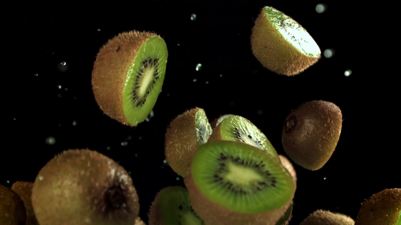 Mitades de kiwi fresco cayendo a cámara lenta con gotas de agua