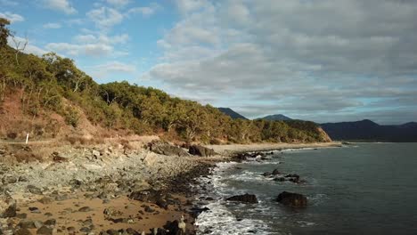 Aerial:-Low-flying-drone-tracks-along-the-coastline-as-a-caravan-drives-past-along-the-captain-cook-highway-between-Cairns-and-Port-Douglas,-in-Far-North-Queensland