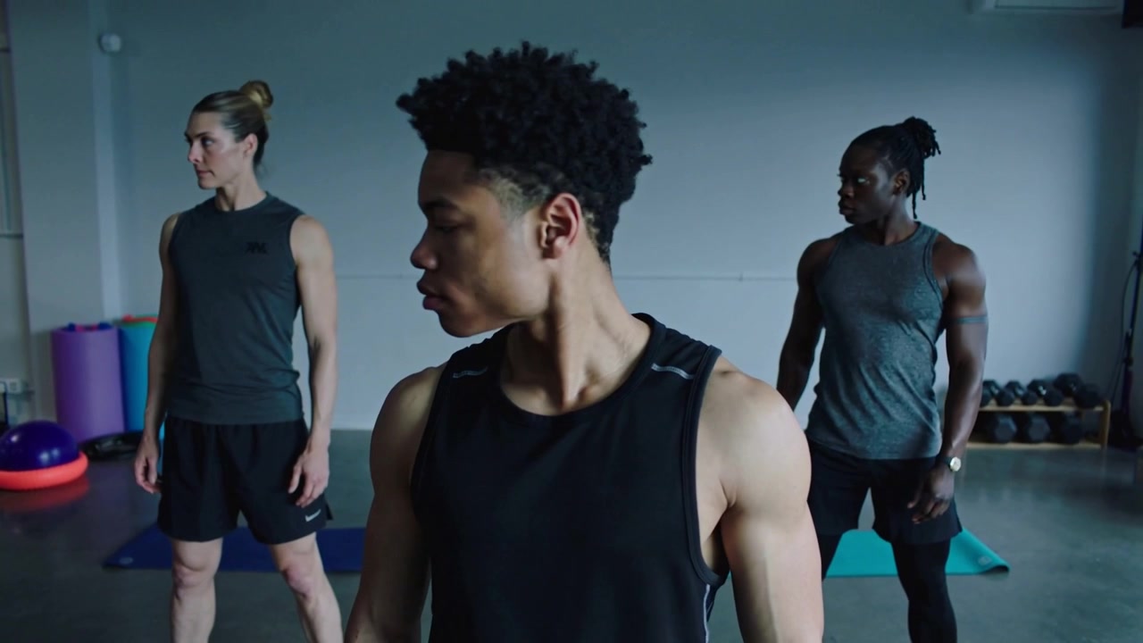 Ein Teenager in ärmellosem Oberteil beginnt und bereitet sich auf seine Routine vor, indem er sich auf Matten im Fitnessstudio dreht und blickt.