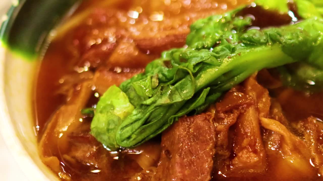 A detailed view of tender stewed meat with fresh greens in a rich, savory broth.