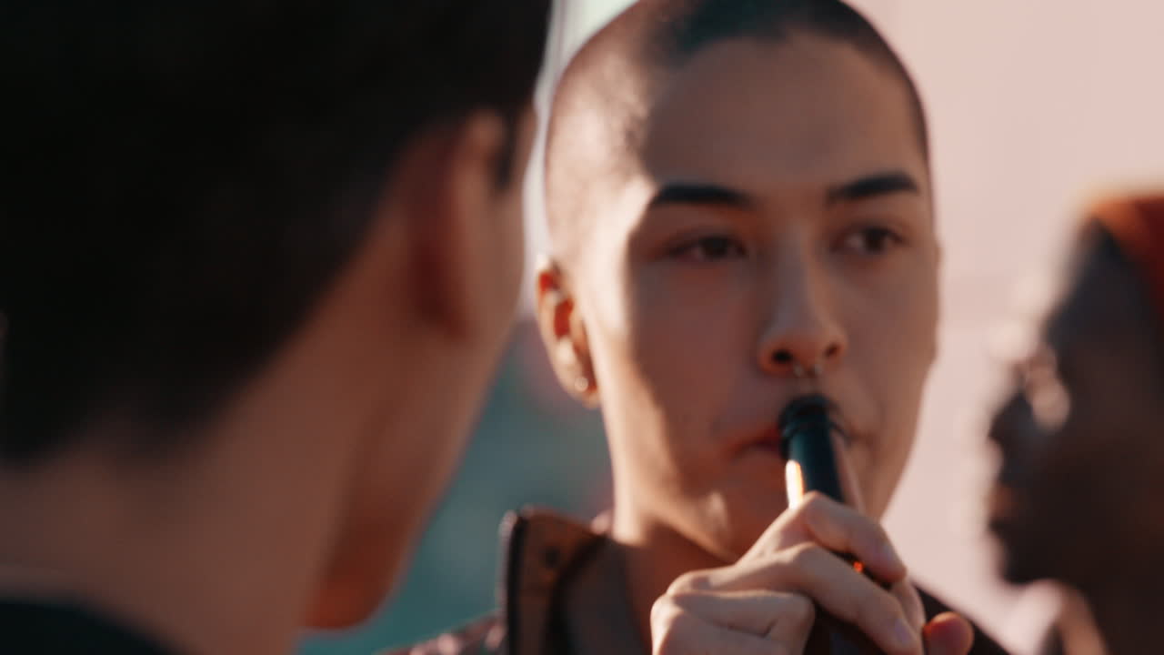 천천히 움직이는 젊은 동성애 커플이 일몰 때 옥상 파티를 즐기고 술을 마시고 친구들과 함께 여름 휴가를 축하하고 있습니다.