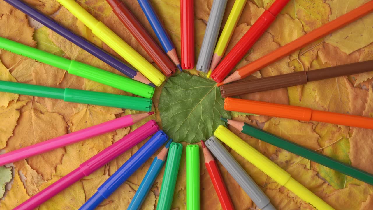 цветные карандаши и маркеры вращаются на фоне желтых осенних листьев.