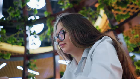 close-up of woman working on phone with decorative lights and greenery in background, capturing a modern workspace, casual business, or digital lifestyle in stylish, vibrant setting