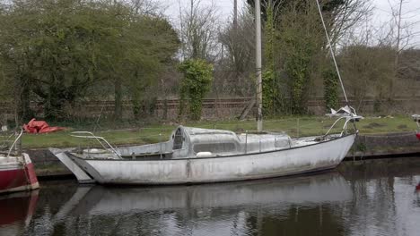 small dirty sailboat moored on narrow rural countryside canal marina