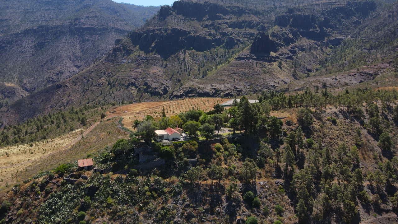 parque natural de tirma, gran canaria: vista aérea en órbita sobre un grupo de árboles y viviendas, viendo grandes montañas