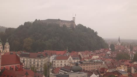 scenic view of ljubljana, slovenia, with historic rooftops, castle hill, and lush greenery under a cloudy sky.