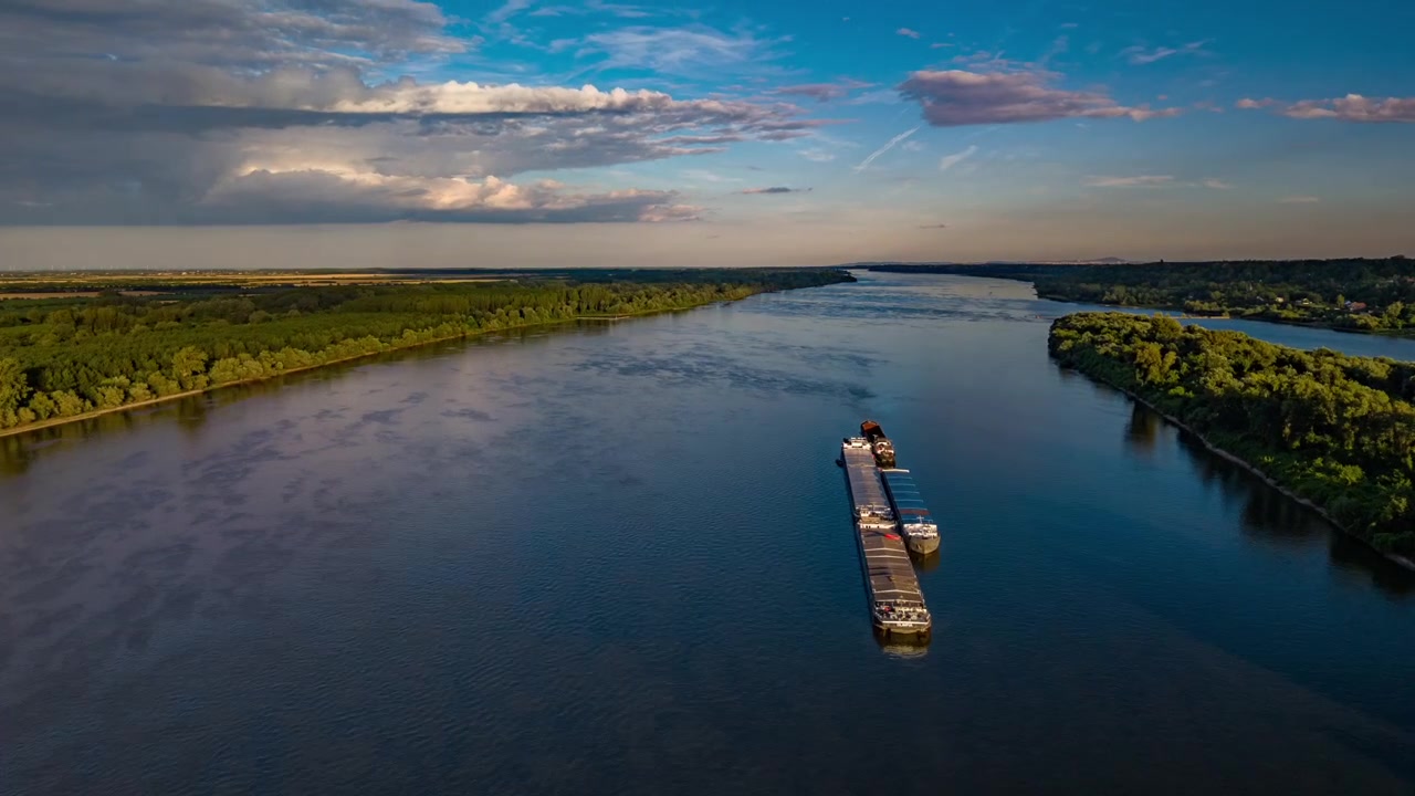 Ripresa aerea di alta qualità con drone di una chiatta da carico commerciale che naviga il fiume Danubio. Navigazione interna, logistica europea, trasporto fluviale: la natura incontra l'industria.