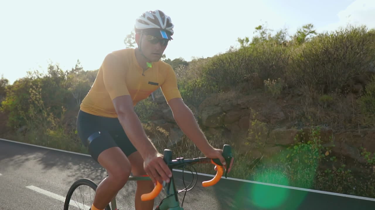 With a clear road ahead, a man rides his road bike in the morning, immersing himself in outdoor exercise. The slow-motion recording magnifies the essence of extreme sports