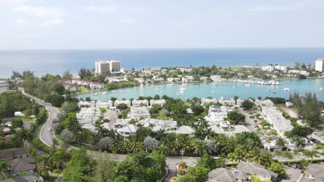 drone footage capturing a sleek car cruising through the upscale community of freeport, montego bay, jamaica. lush greenery, ocean views, and luxury villas line the scenic, well-paved road