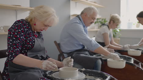 a female potter's wheel sculpting teacher explains how to work and teaches an elderly woman to work with clay and make mugs and jugs. master class for pensioners. pottery courses