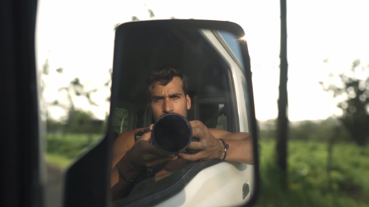 A man takes a selfie reflected in the side mirror of a car, with a camera obscuring his face. The background shows the lush, green landscape of La Fortuna, Costa Rica