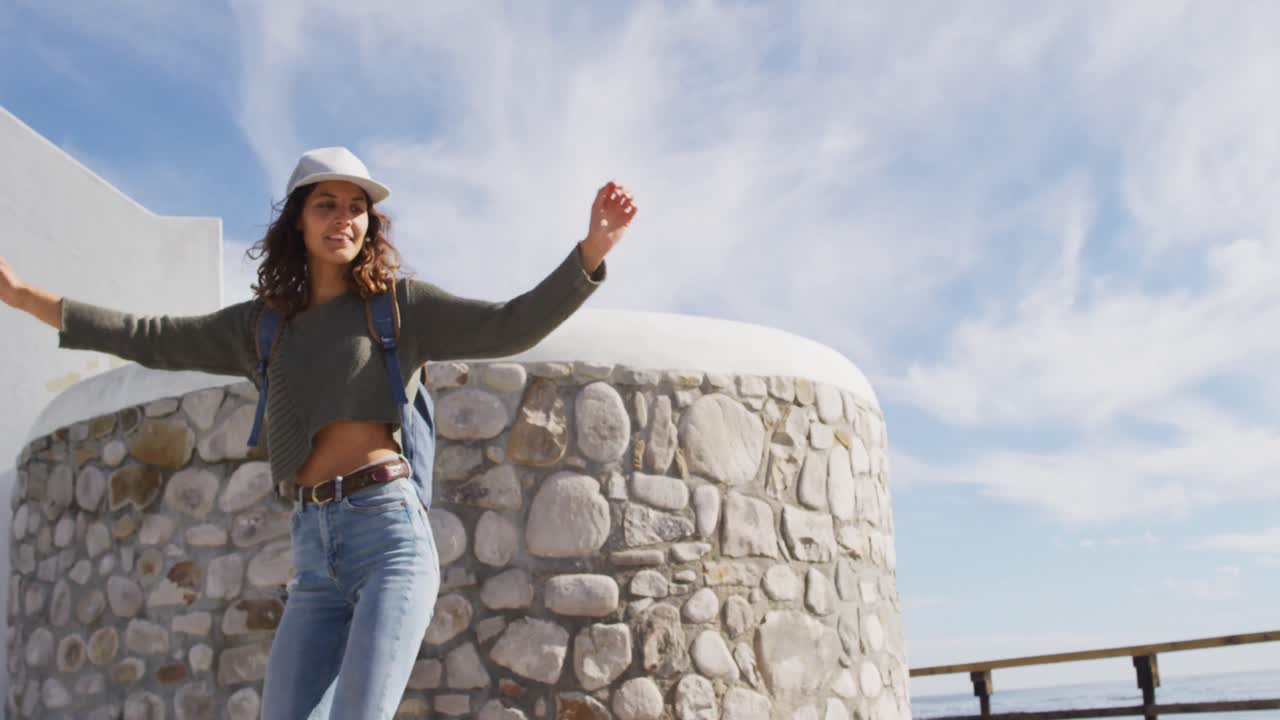 feliz mujer de raza mixta patinando con los brazos en el aire y sonriendo en el soleado paseo marítimo por el mar