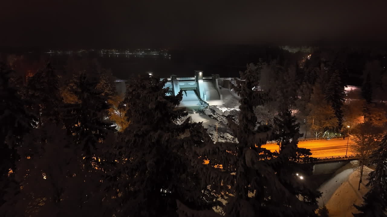 Aerial view over trees, revealing the Imatrankoski dam, winter night in Finland