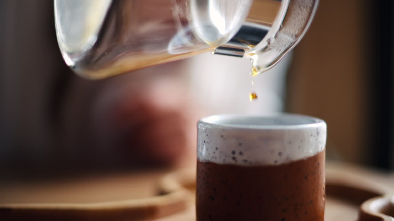 Close up of a woman pouring coffee in a cup from a glass pot standing on a wooden tray