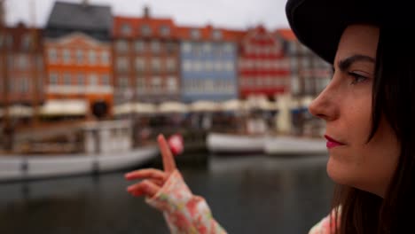 Close-up-on-face-of-woman-pointing-at-typical-Danish-houses-with-her-finger,-Nyhavn