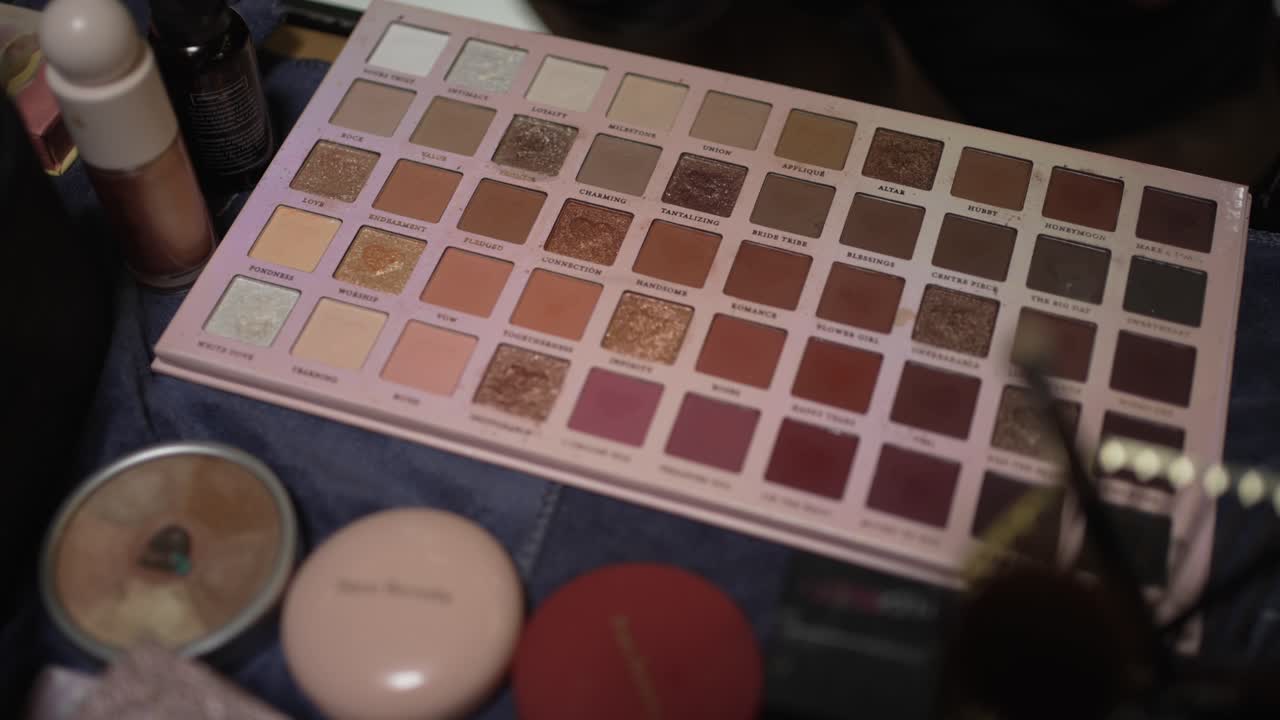 open makeup palette with warm earth toned shades next to compact powders and brushes