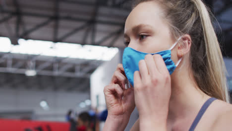 mujer caucásica en forma ajustando su máscara facial en el gimnasio