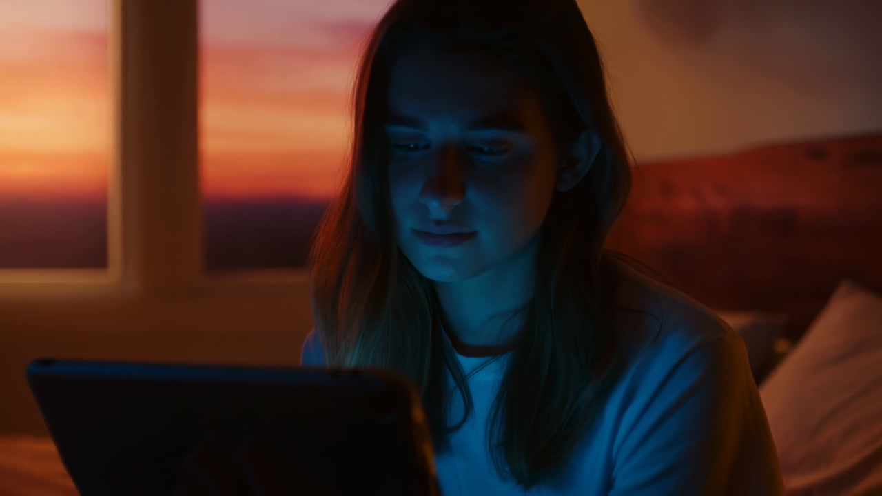 Sunset Window Glow With White Woman Seated On Bed Holding Tablet, Blue Screen Lighting Face, Focused