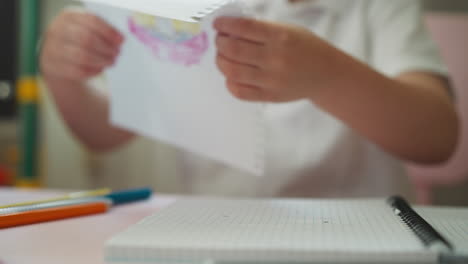 boy pulls to tear out notebook page with drawing at table