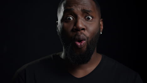 Emotional afro guy posing indoors. Male person saying wow on black background