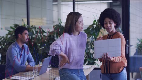animation of statistical data processing against two diverse women over a laptop at office