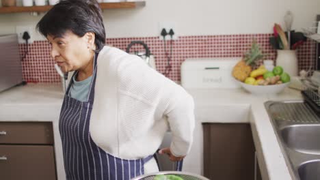 senior biracial woman wearing blue apron in kitchen alone