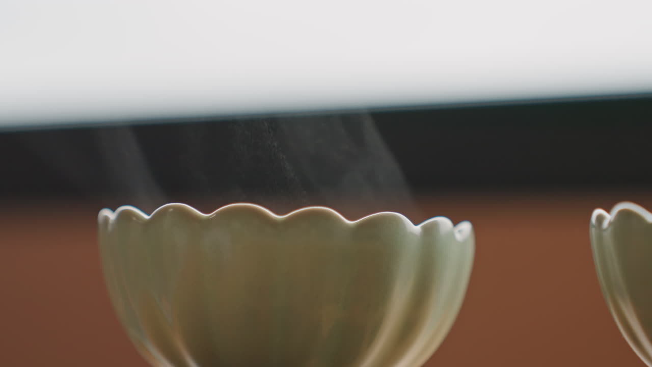 Scène de tasse en céramique. La lumière douce met en valeur la scène paisible de la tasse. Une légère vapeur s'élève au-dessus de la réconfortante boisson en céramique. Ambiance calme et apaisante dépeinte par la tasse de café vaporeuse sur le rebord de fenêtre.