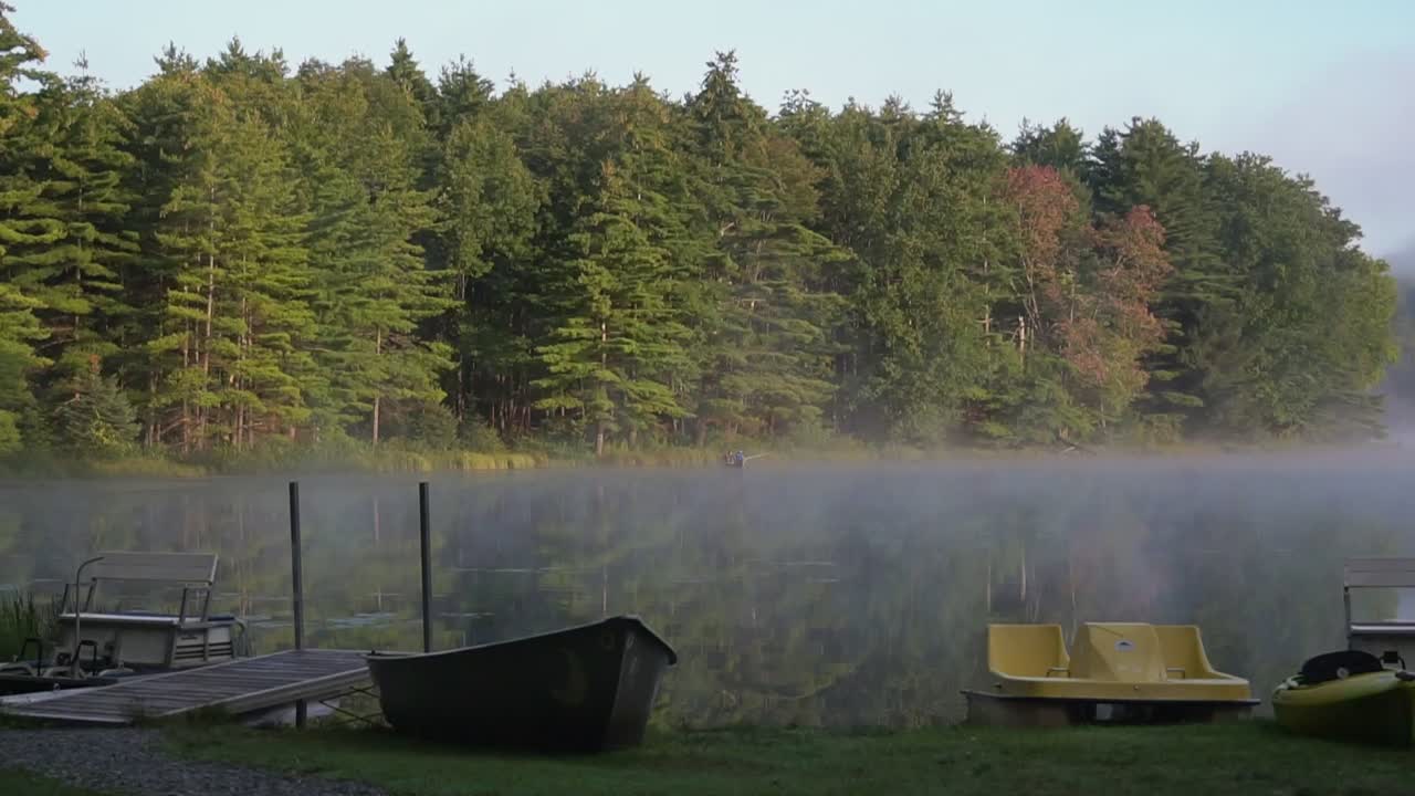 Foggy morning as dew and mist floats over a calm serene pond
