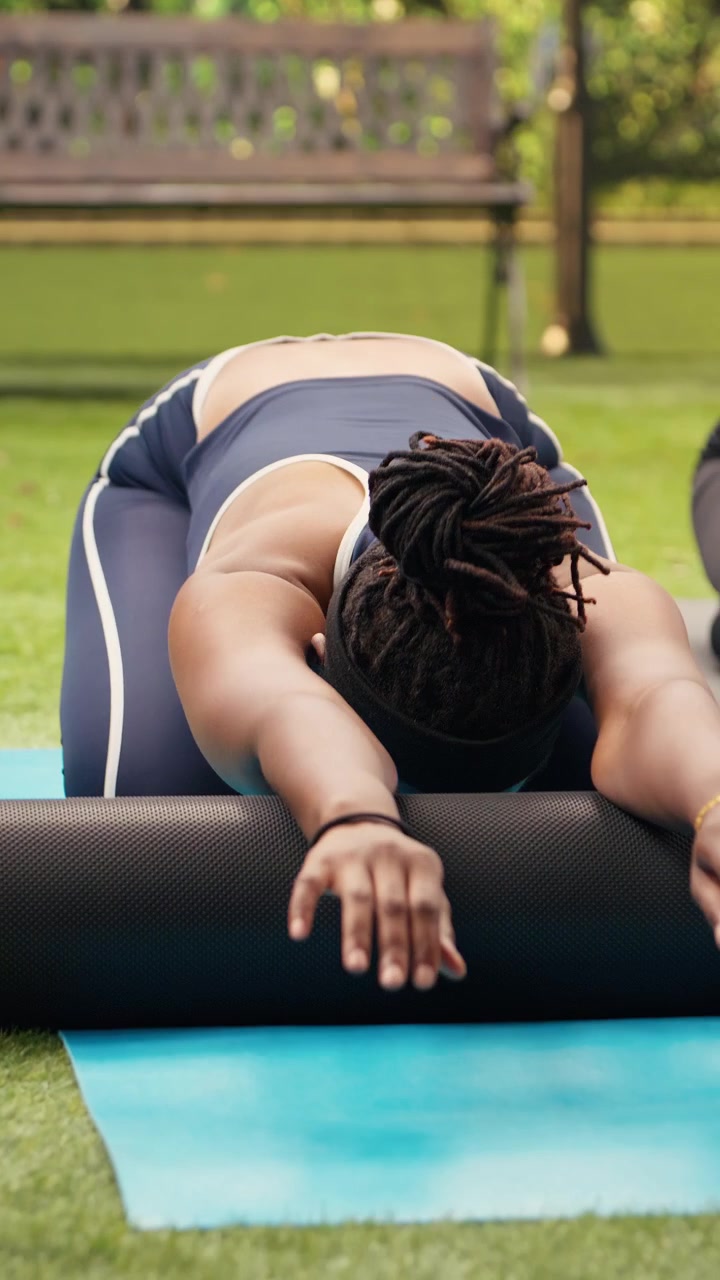 Vertical Video Participants sitting in child pose on foam roller on yoga mat