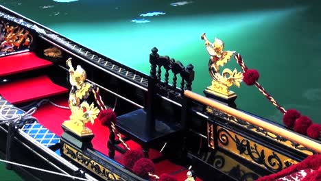 close up of the interior of a venetian gondola with golden statues and red carpet moored in the aqua blue waters of a canal