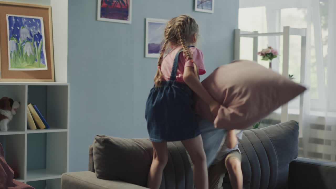 Happy elder sister and brother have pillow fight at home