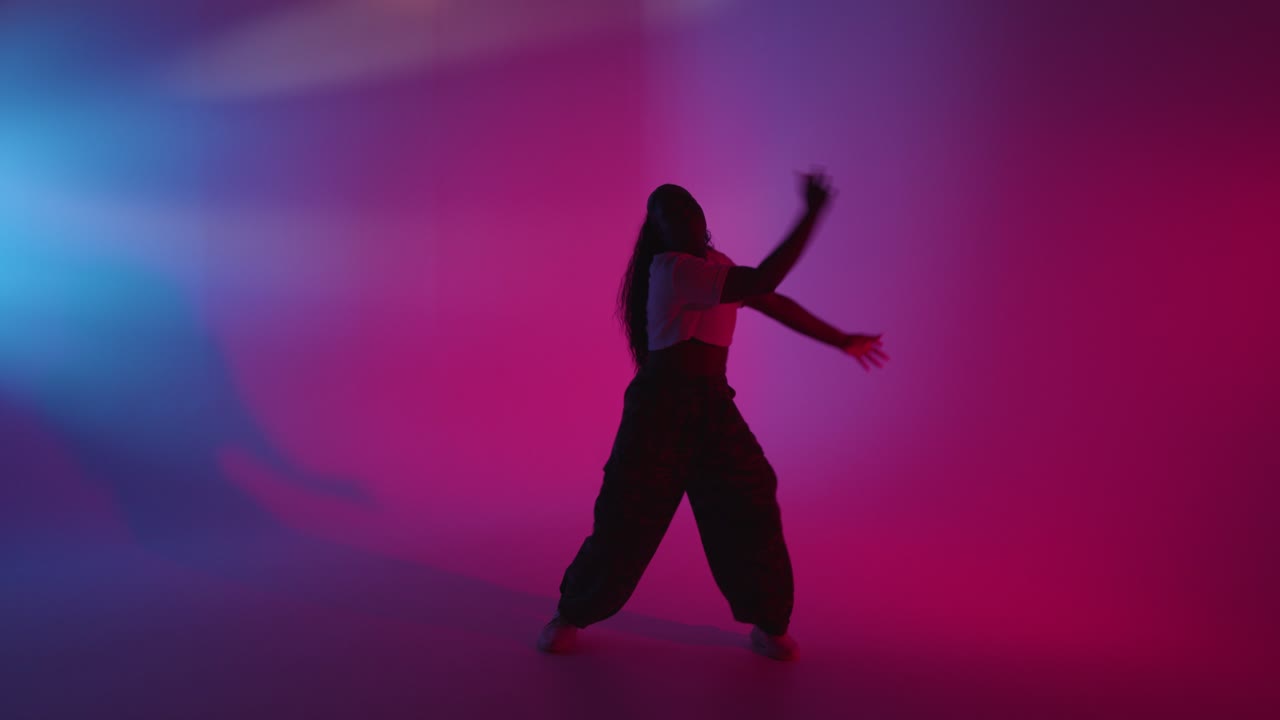 Full Length Studio Shot Of Young Woman Dancing Against Blue And Pink Lit Background