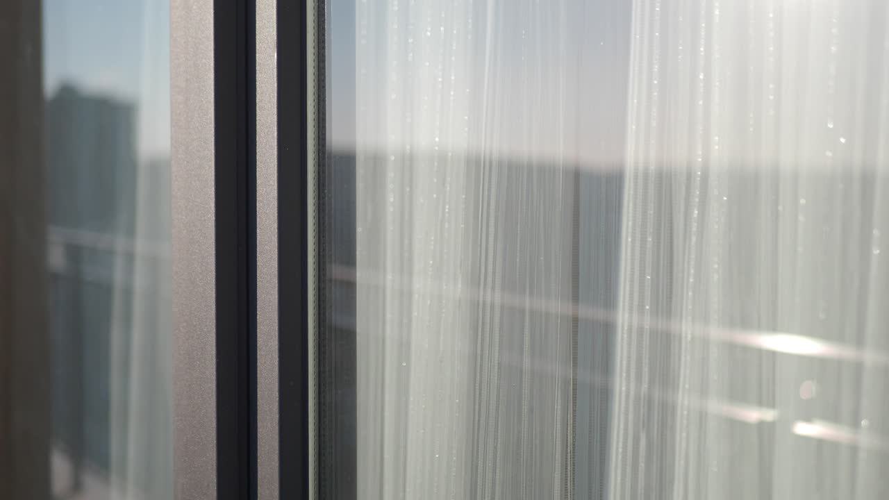 Close up of a window with white curtains and a reflection of a city outside
