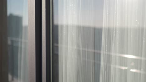 close up of a window with white curtains and a reflection of a city outside