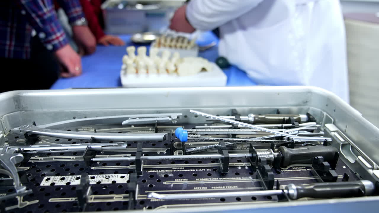 Large box with multiple medical tools and devices. Unrecognized man in white robe displays the model of spine.