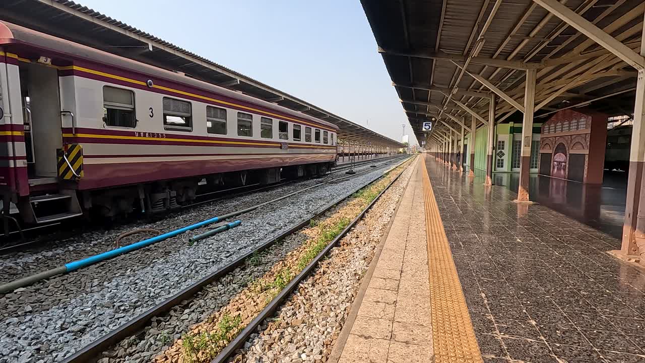 Lenta ripresa diurna con carrellata di un treno passeggeri in partenza dal binario coperto di Bangkok, linee prospettiche marcate