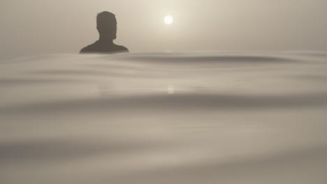 unrecognizable surfer silhouette sitting on surfboad wainting for the swell, mystic atmosphere in slow motion