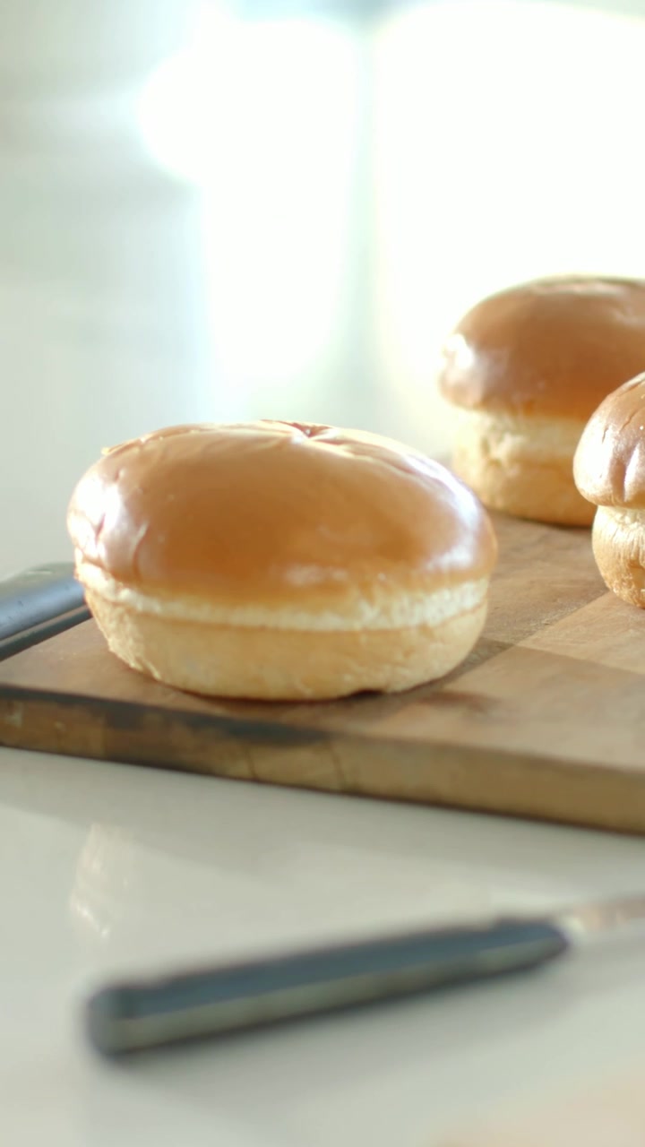 Vertical video: Racking focus, camera bringing knife and slice forward on counter, buns softening