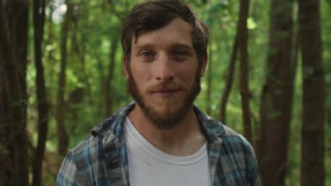 expressive bearded young man looking straight in to the camera with forest background