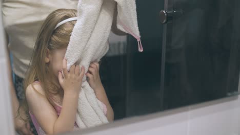 cute girl wipes face by mother holding towel at mirror