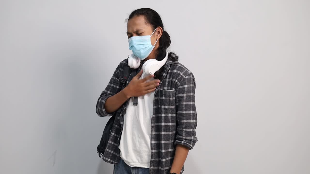 Giovane studentessa universitaria asiatica malata che indossa una mascherina di protezione e tossisce, con febbre a causa del coronavirus 2019 o COVID-19. Concetto di Coronavirus