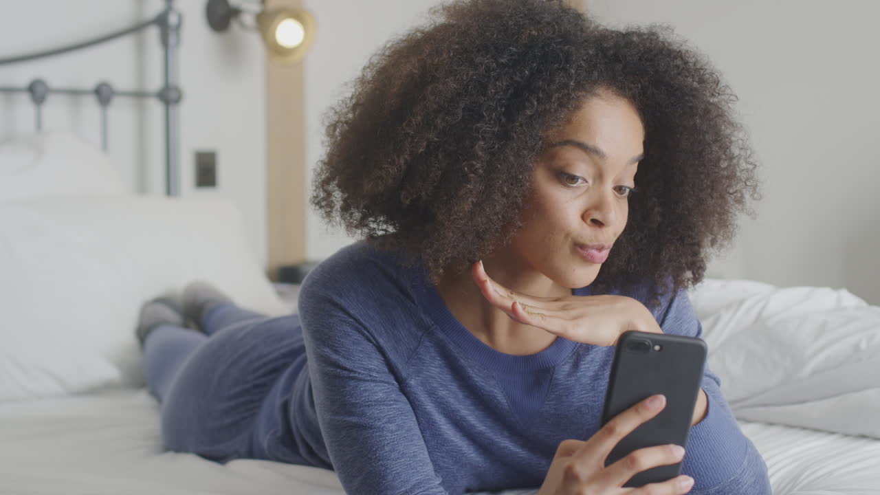 Mulher vestida posando e tirando selfies com o celular deitada na cama