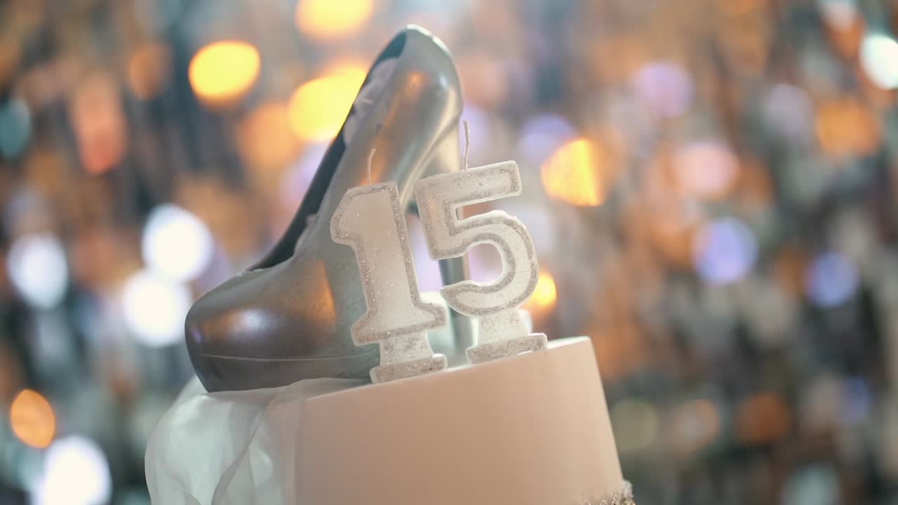 Rivelazione graduale di un'elegante torta di compleanno per i quindici anni che mette in risalto una scarpetta argentata e una decorazione con il numero quindici, con illuminazione bokeh calda, scarsa profondità di campo e un'atmosfera da festa glamour