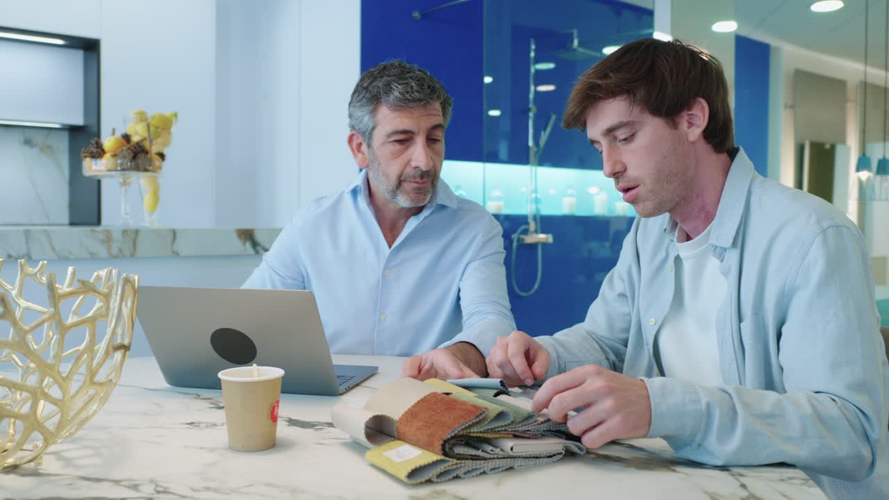 Men discussing fabric samples at a table with a laptop