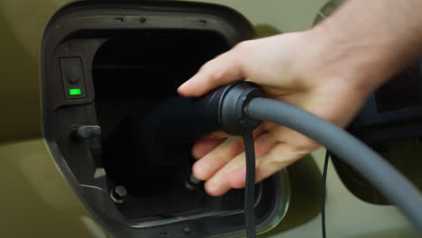 extreme close up of driver opening charging port flap, plugging electric car