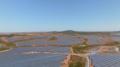 Drone-dolly-above-solar-farm-fields-and-wind-farms-in-the-distance