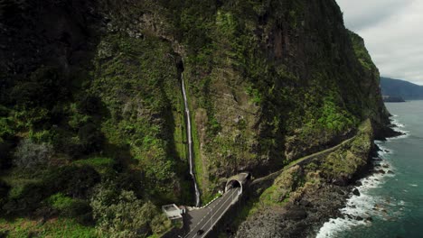 Drone-Footage-of-Large-Waterfall-Next-to-the-Road,-Car-Driving,-Steep-Mountain,-Ocean,-Madeira-4k